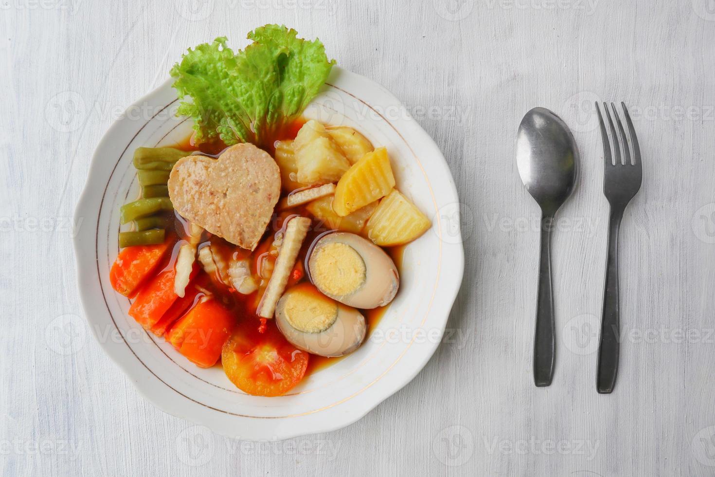 selat solo é uma salada tradicional da indonésia. feito de ovos cozidos, grão de bico cozido, cenoura cozida, batatas fritas e alface, bife ou bistik. servido na mesa de madeira foto