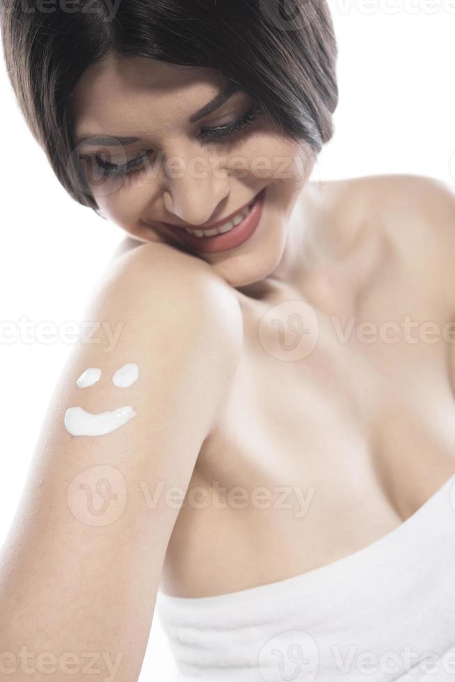 linda mulher de pele aplicando loção corporal em fundo branco foto