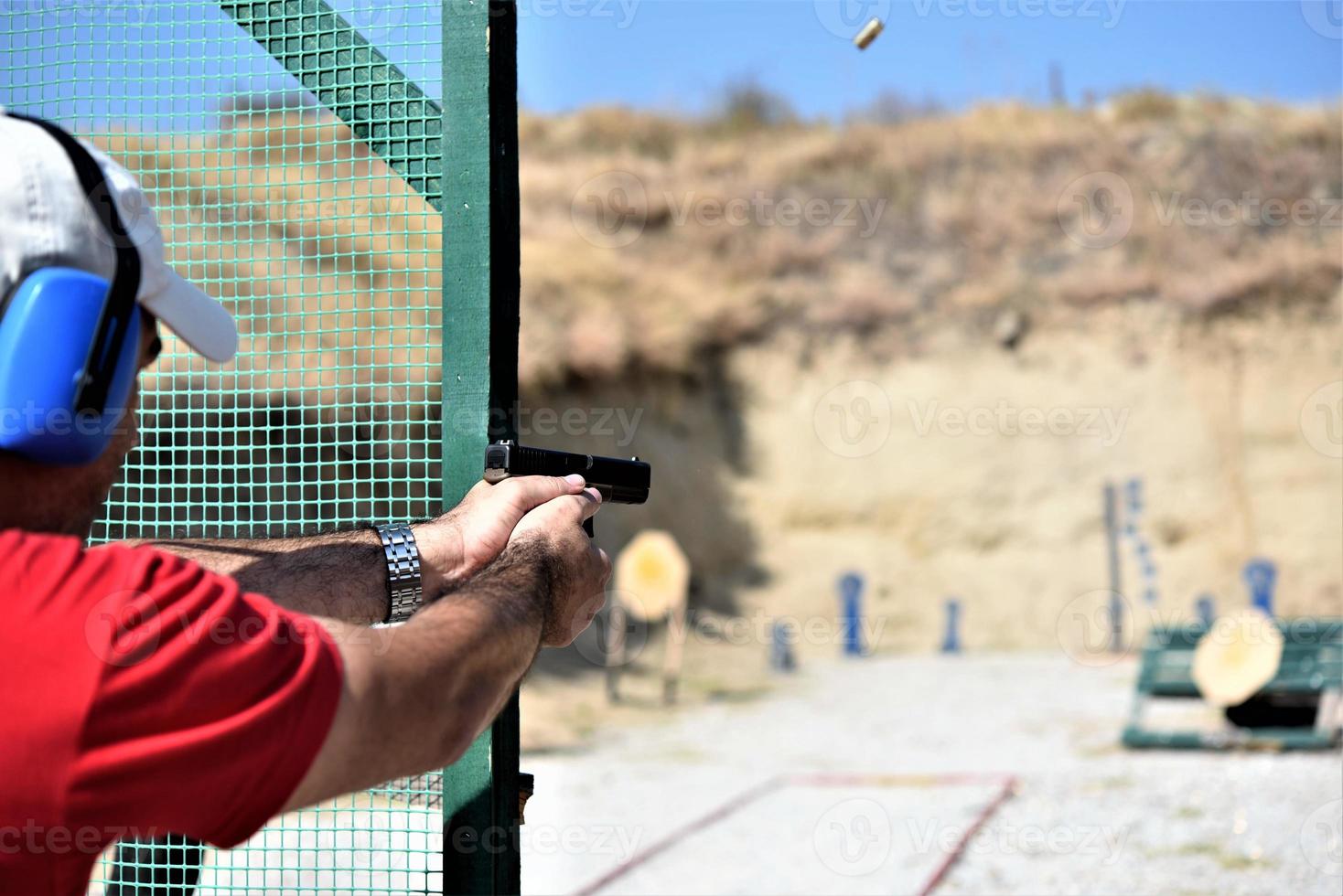 vista traseira de um homem disparando sua arma em um rancho de prática. foto