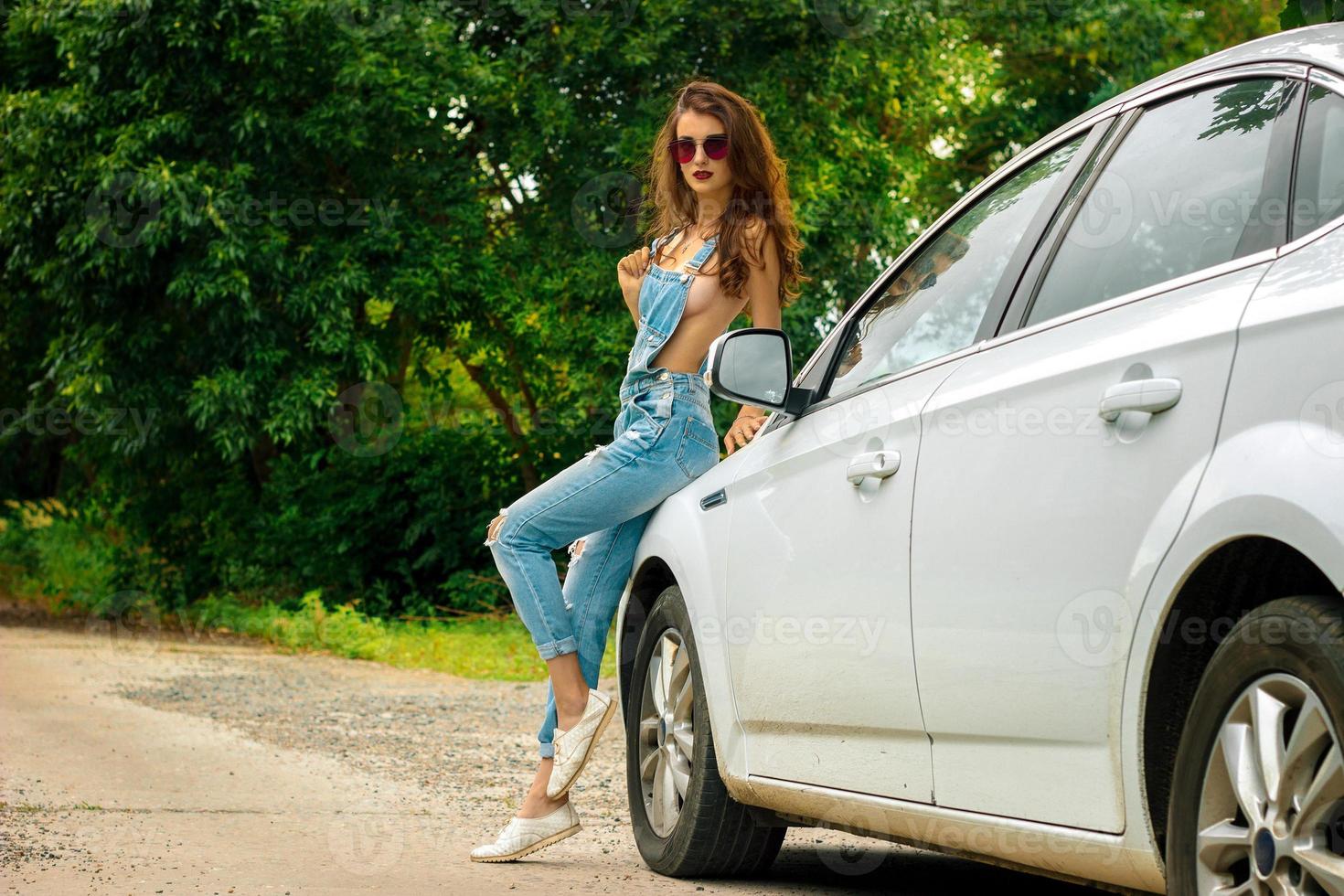 morena jovem e sexy de macacão jeans em um carro branco foto