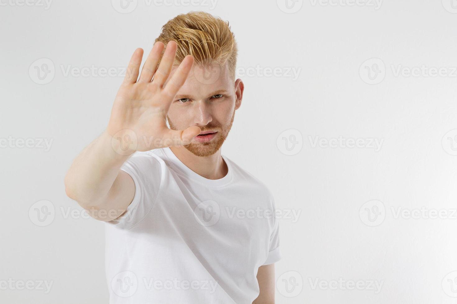 pare o sinal das mãos. jovem em branco modelo camiseta branca mostrando o gesto de parada. cara de barba ruiva e vermelha isolado. conceito de proteção de perigo. copie o espaço e zombe na camiseta. foco seletivo foto