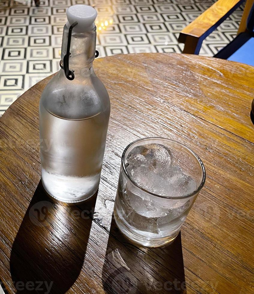 refrescante vodka gelada na garrafa com pedras de gelo no copo servido no pub foto