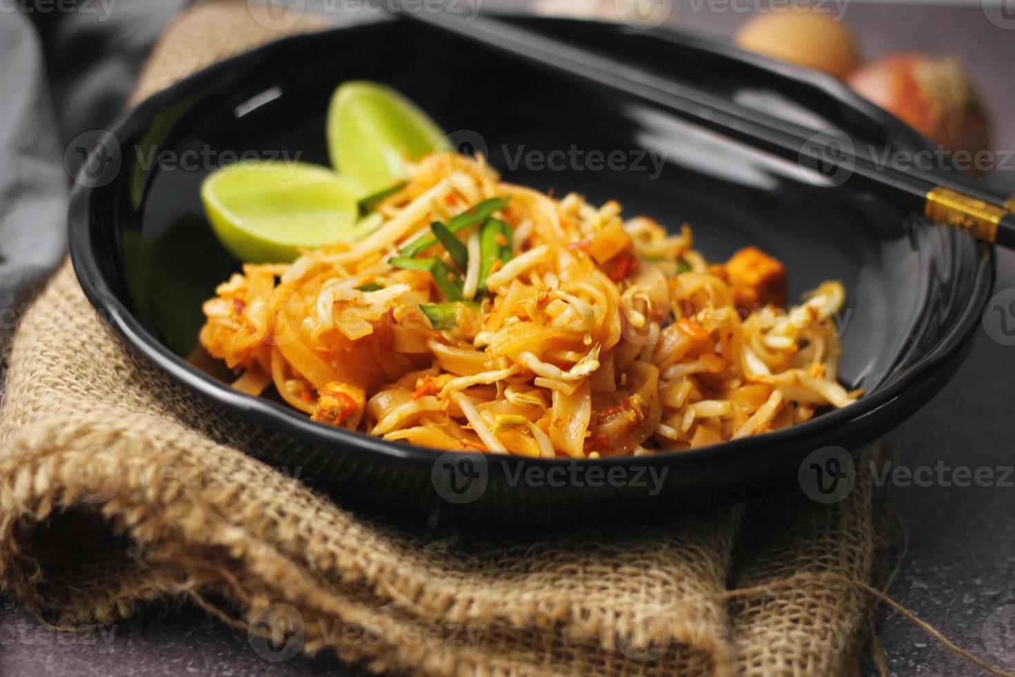 pad thai ou pad thai estilo tailandês servido com limão e temperos em um prato preto, é um alimento que pode ser encontrado na comida de rua da tailândia. foto