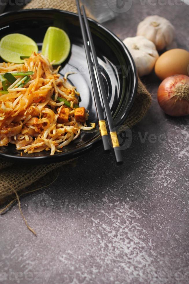 pad thai ou pad thai estilo tailandês servido com limão e temperos em um prato preto, é um alimento que pode ser encontrado na comida de rua da tailândia. foto