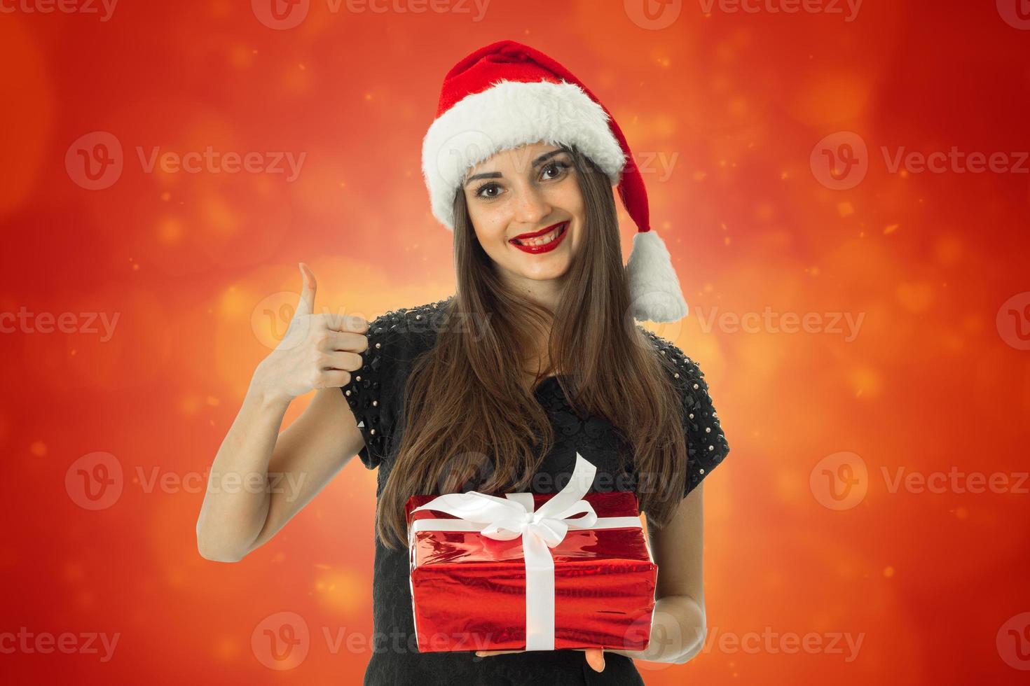 menina sorrindo com chapéu de Papai Noel com presente vermelho foto