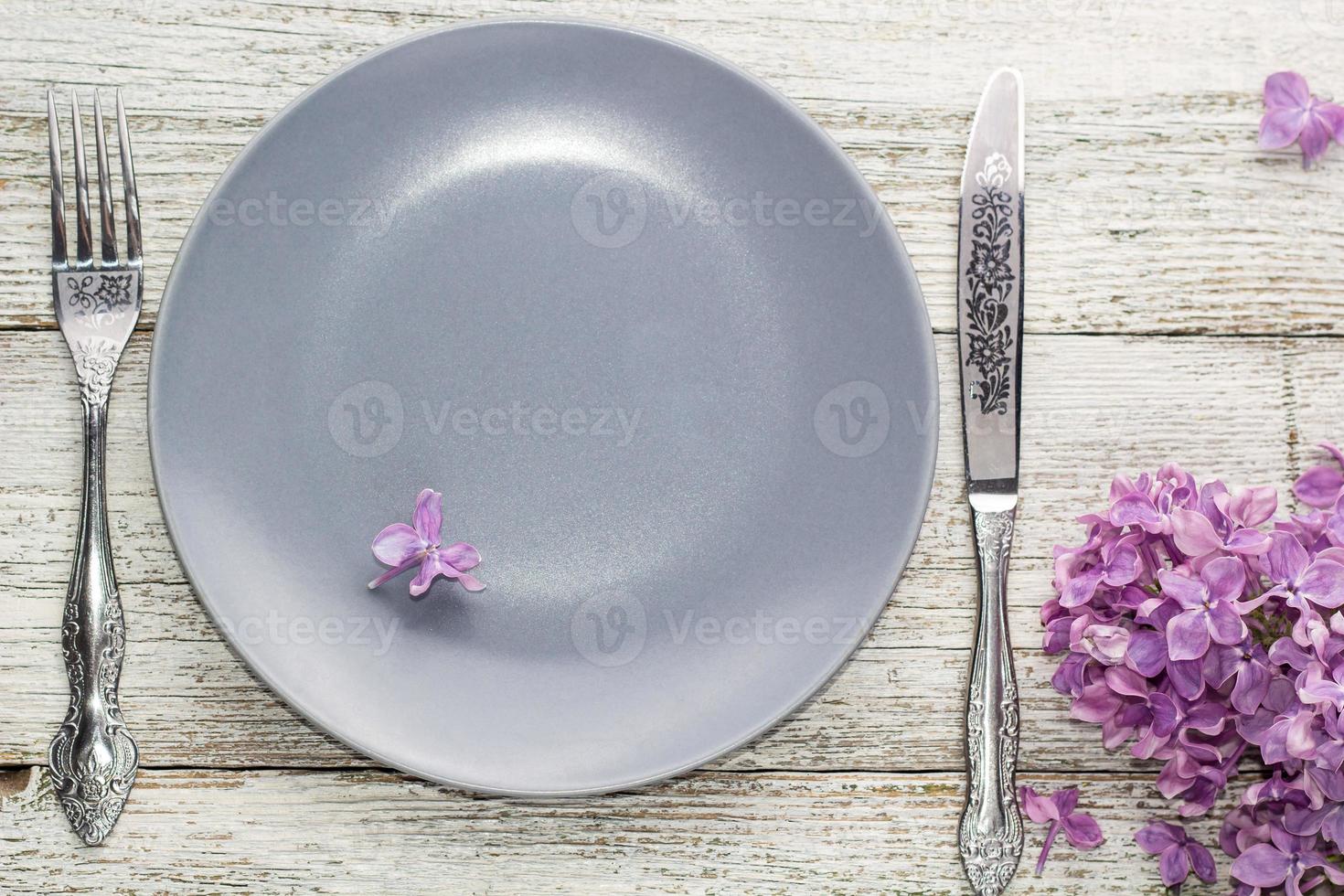 configuração de mesa de primavera com garfo de prato e faca decorada com flores lilás em fundo branco de madeira foto