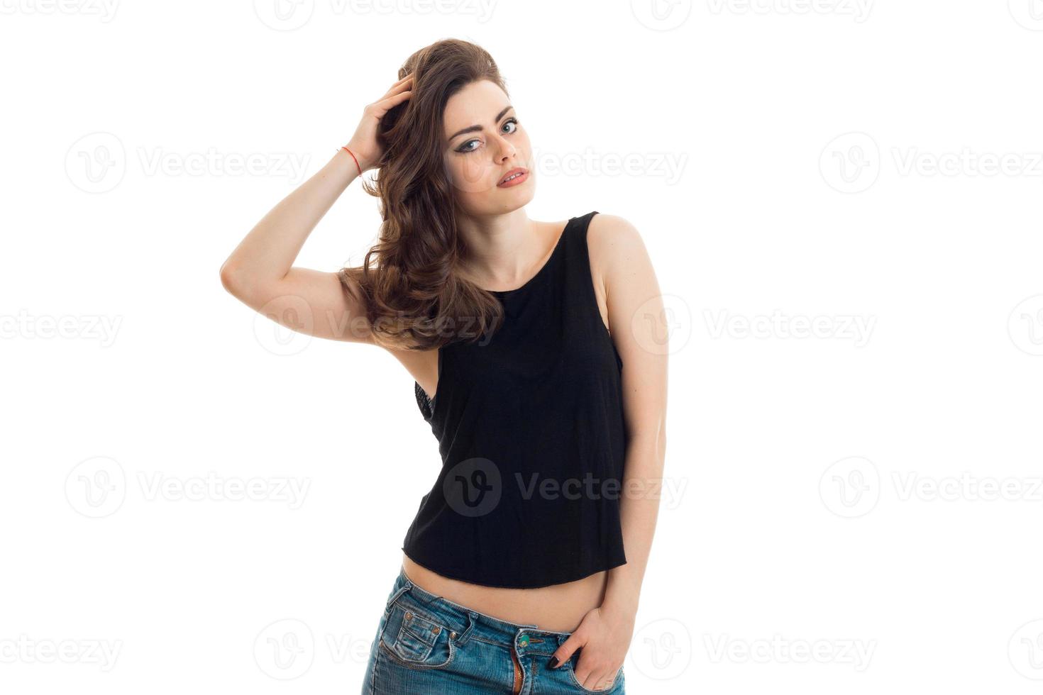 incrível jovem morena em camiseta preta olha para a câmera e segura o cabelo da mão foto