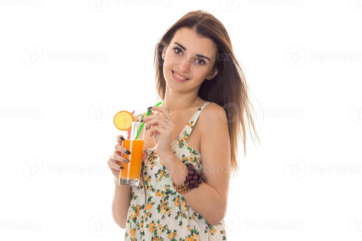 jovem linda menina morena em sarafan com padrão floral bebe coquetel de laranja e sorrindo para a câmera isolada no fundo branco foto