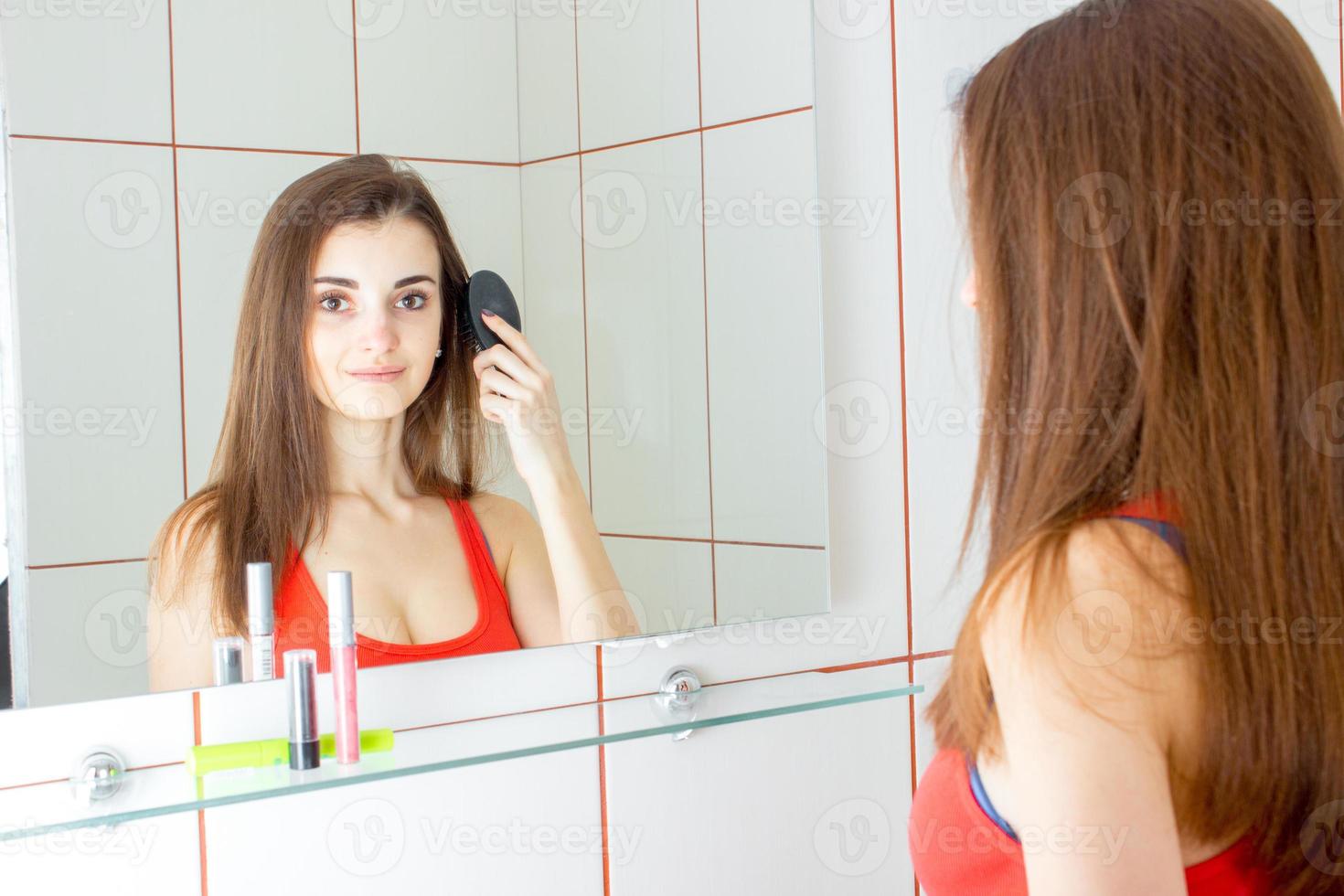 jovem sorridente se olha no espelho e penteia o pente de cabelo foto