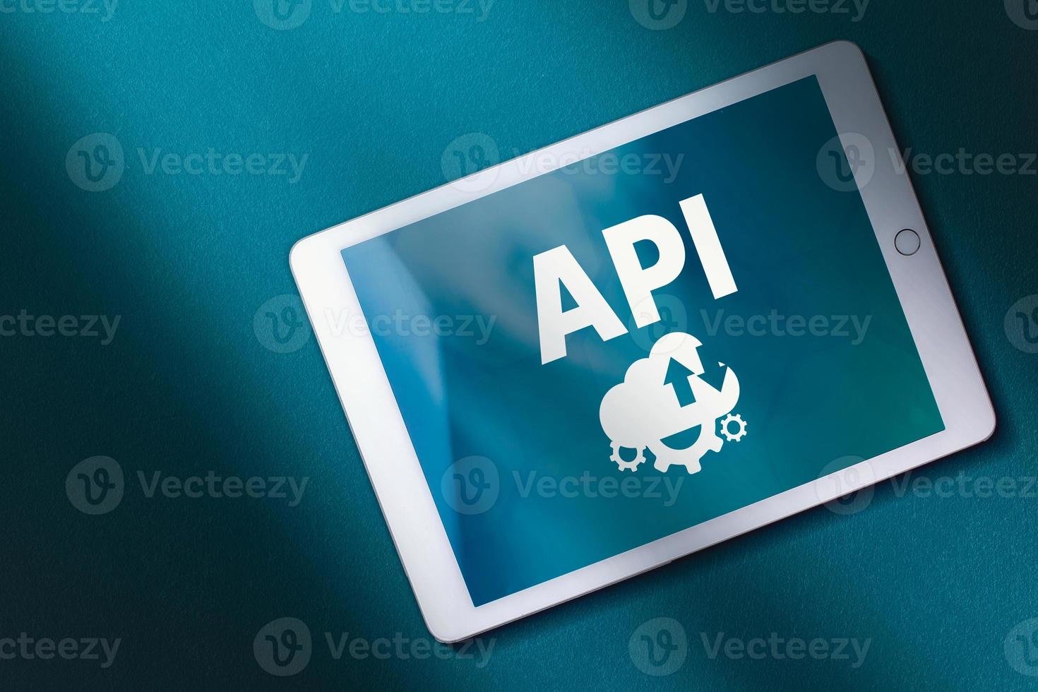 vista superior do tablet digital com palavra de sigla api na tela e fundo azul-petróleo. copie o espaço. conceito de internet e tecnologia. negócios, programação, interface, aplicação e rede. foto