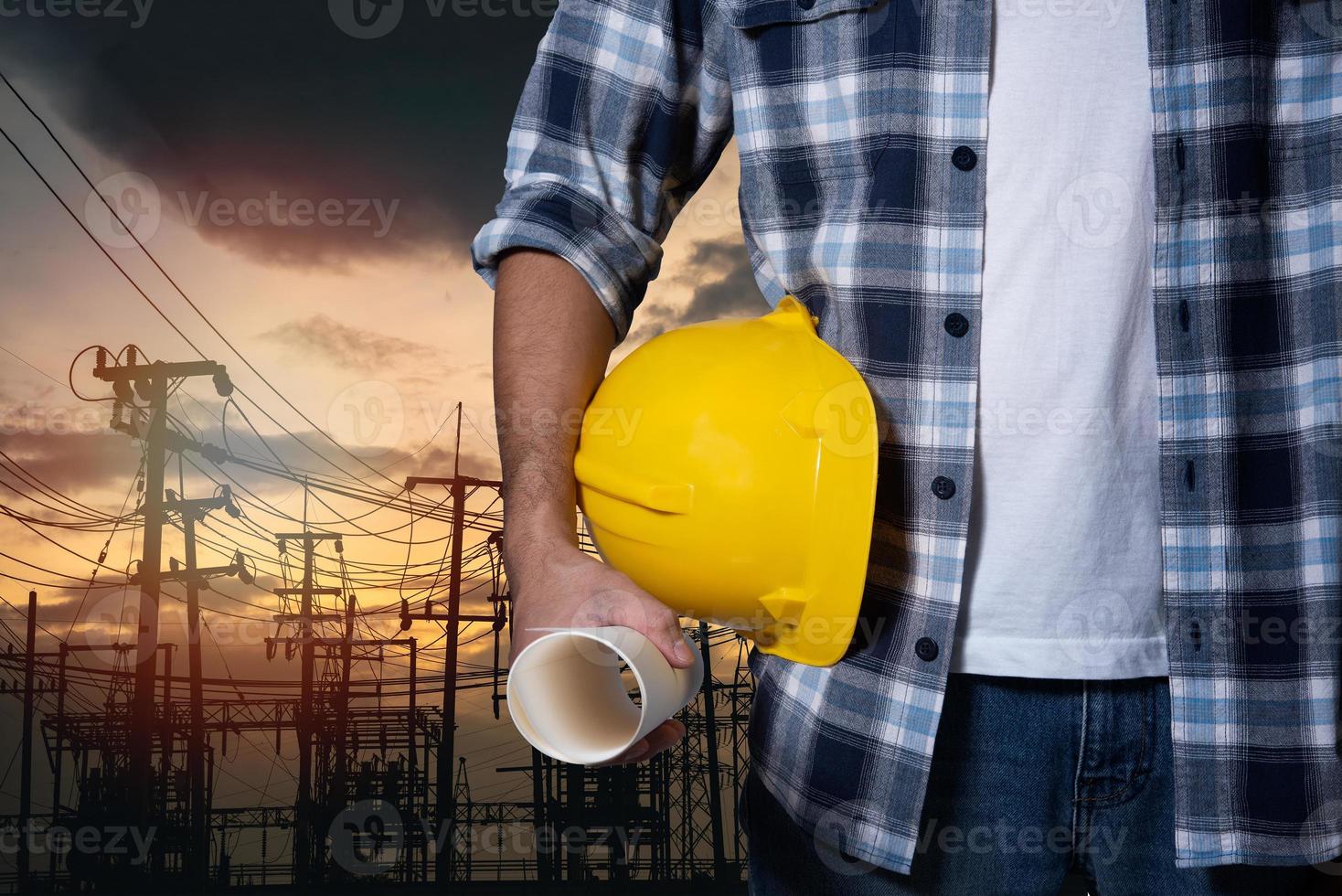 mão de construção de homem engenheiro segurando o capacete de segurança amarelo no poste elétrico no fundo do pôr do sol da usina. capacete de trabalhador engenharia de construção civil. feche a mão do engenheiro segure o capacete de segurança. foto