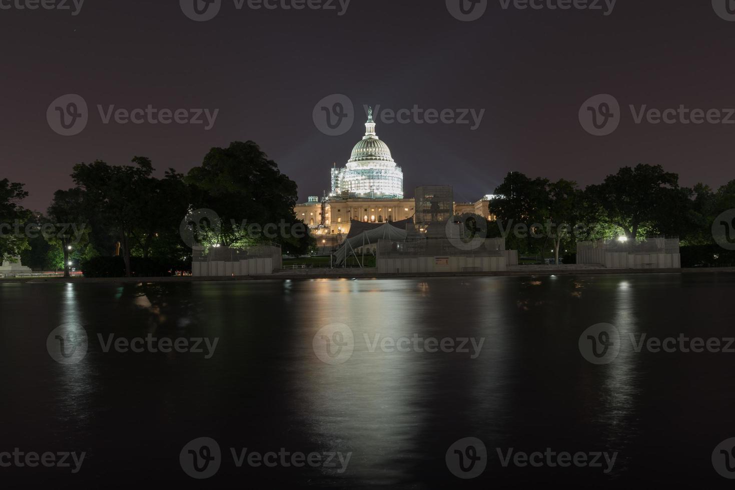 o prédio do capitólio dos eua sob um andaime visto do outro lado do espelho d'água à noite em washington, dc. foto