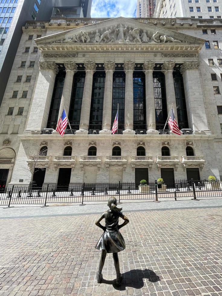 cidade de nova york - 18 de abril de 2021 - estátua de garota destemida olhando para o prédio da bolsa de valores de nova york em wall street em manhattan, cidade de nova york, eua. foto