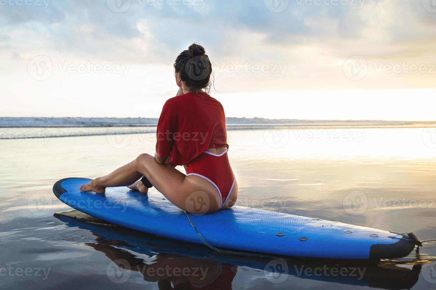 mulher sentada na prancha de surf na praia após sua sessão de surf foto