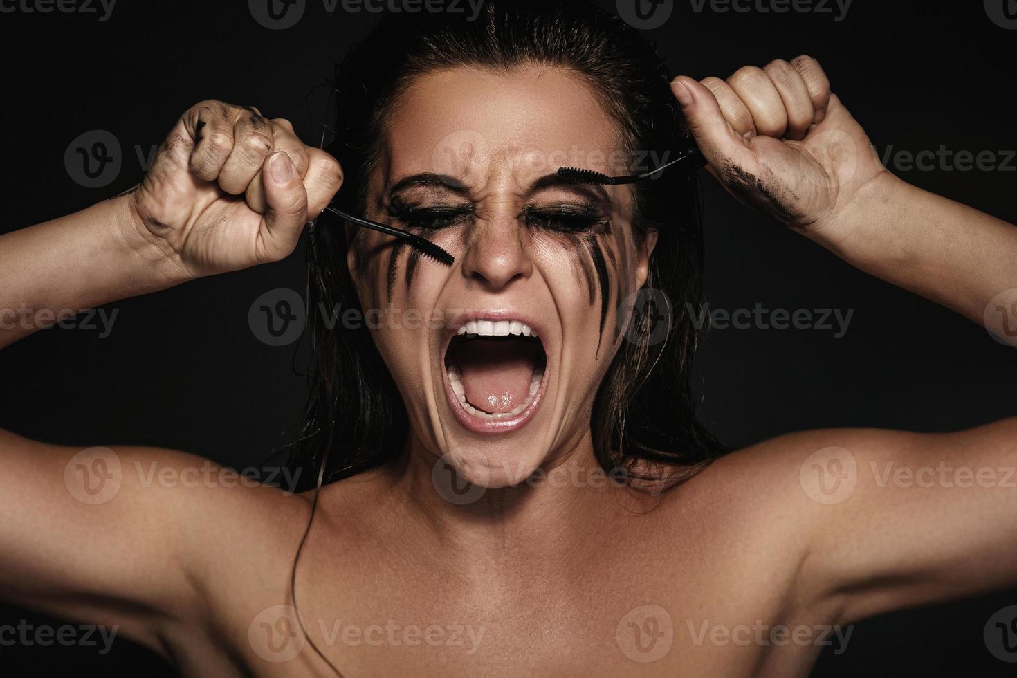 mulher com manchas de maquiagem no rosto e pincéis de rímel quebrados foto