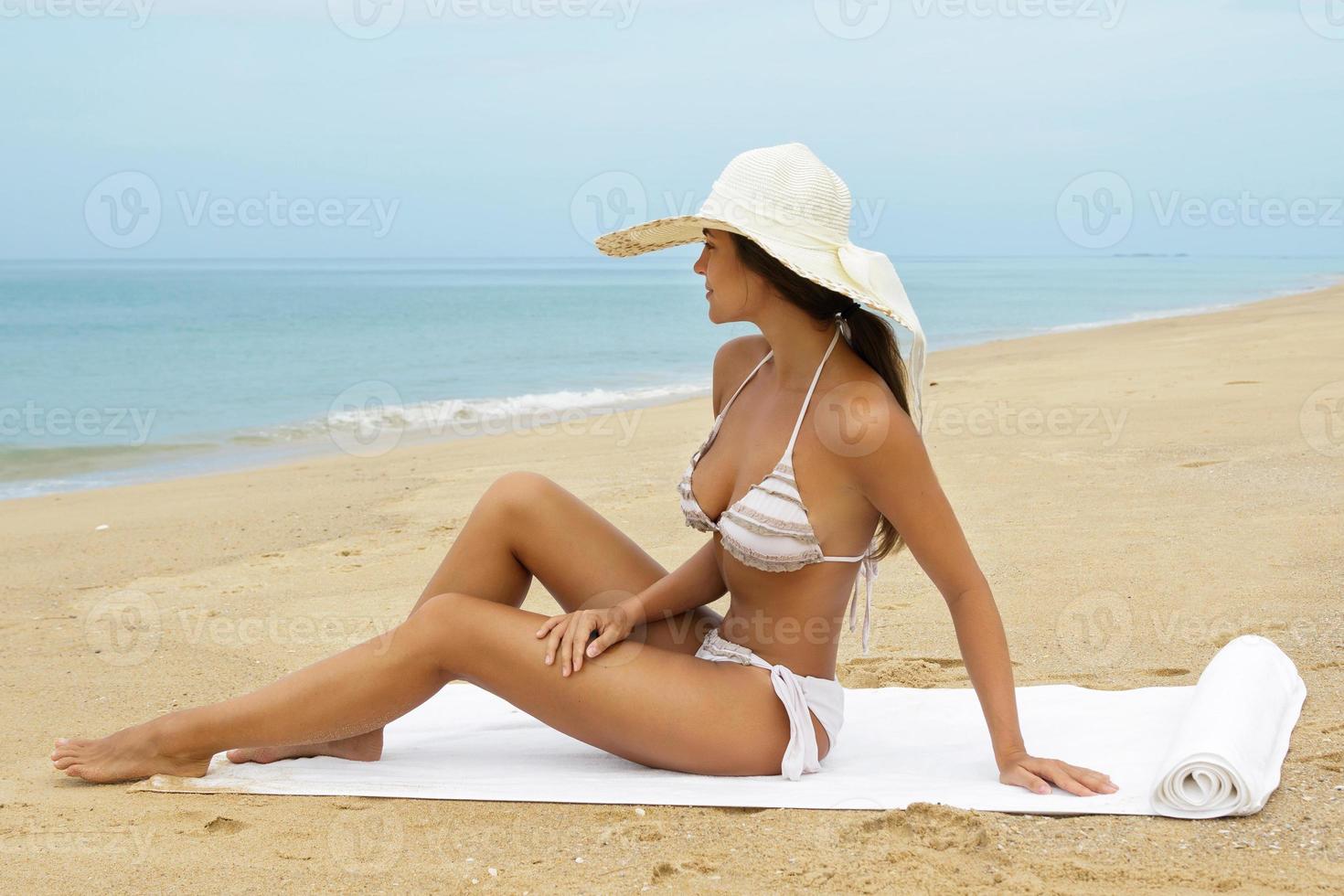 mulher usando chapéu de praia está sentada ao lado de um mar foto