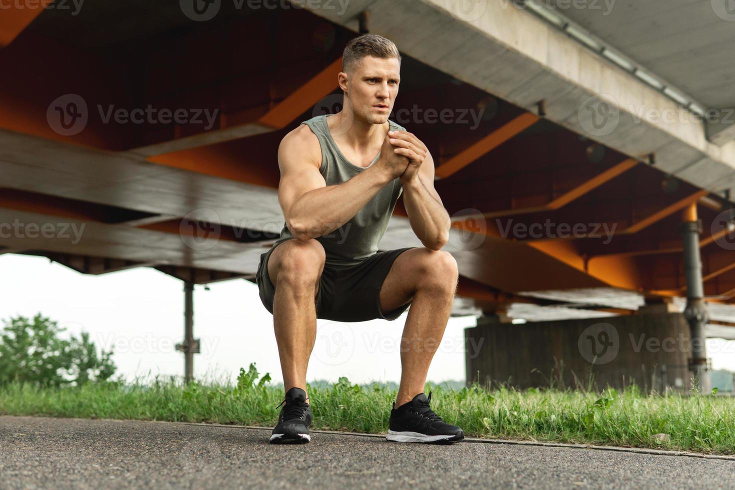 homem musculoso está fazendo agachamento debaixo da ponte durante seu treino de rua foto