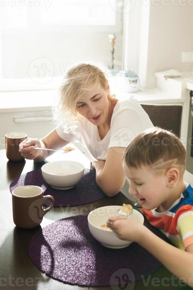 linda mãe e seu filho fofo comendo flocos de milho saudáveis no café da manhã foto