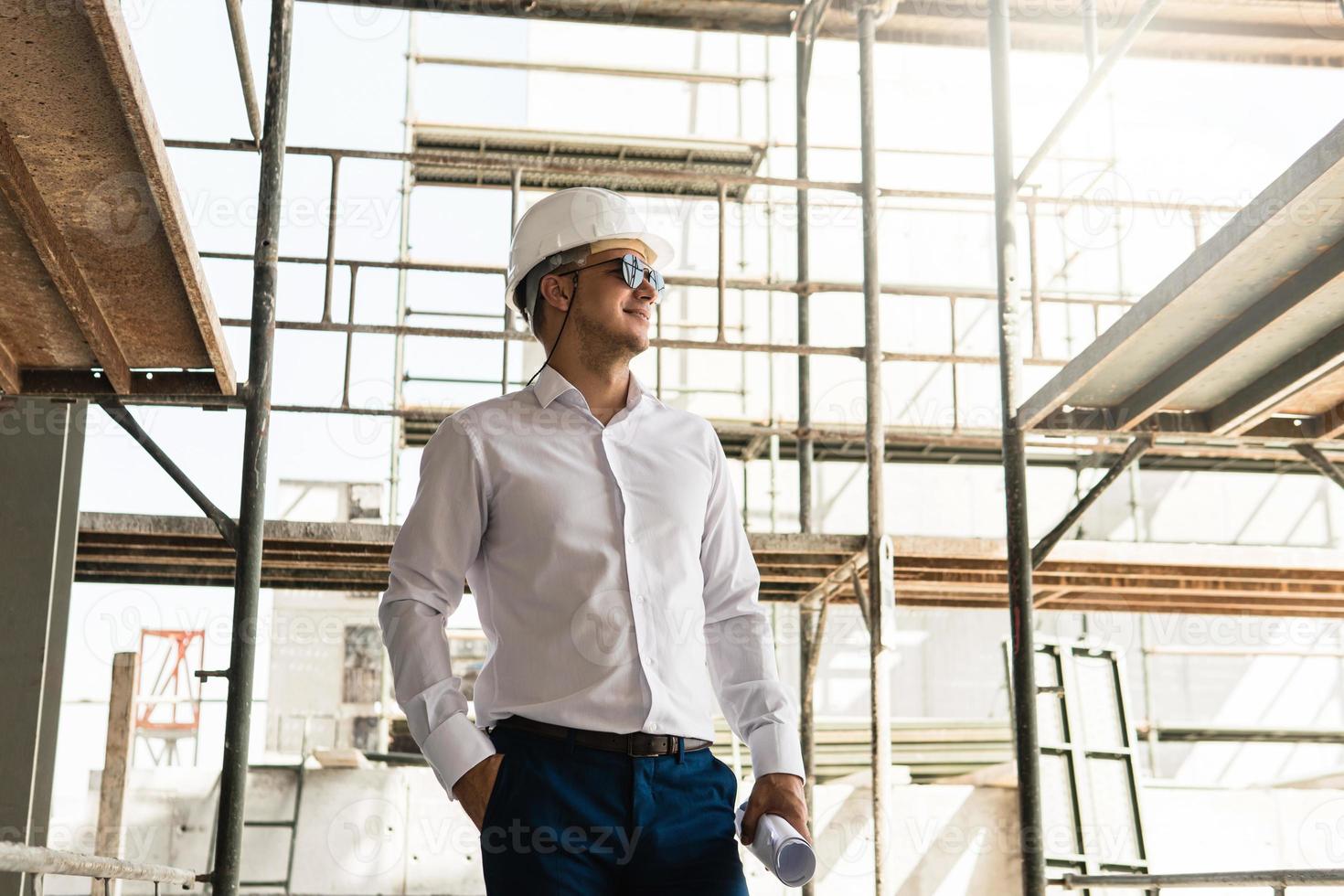 arquiteto de homem ou empresário usando capacete e segurando plantas em um canteiro de obras foto