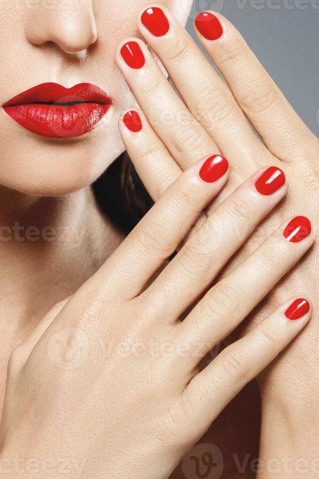 close-up da boca feminina e unhas com batom e manicure vermelho. foto