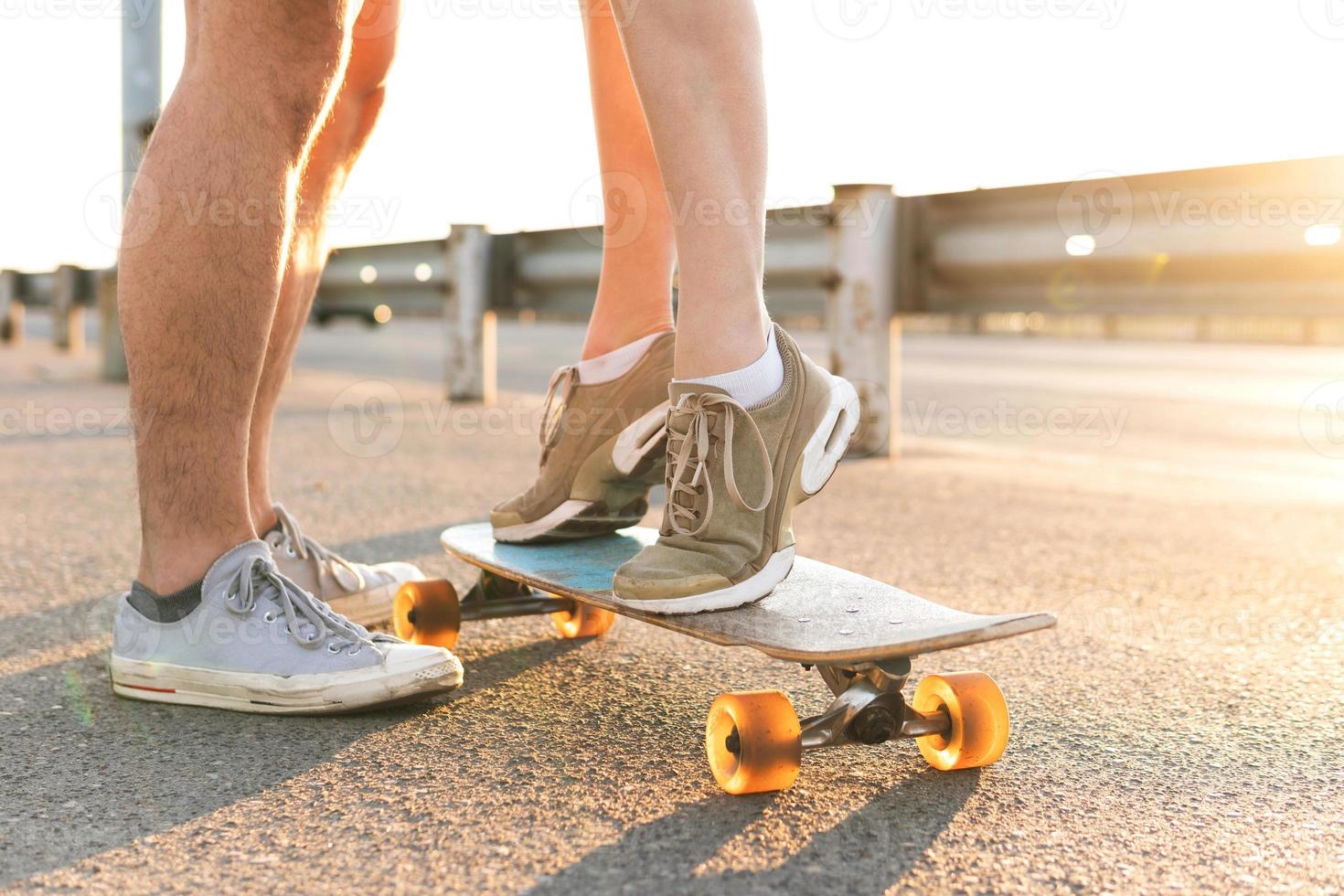 garota de pé em um longboard ao lado do namorado na rua ao pôr do sol foto