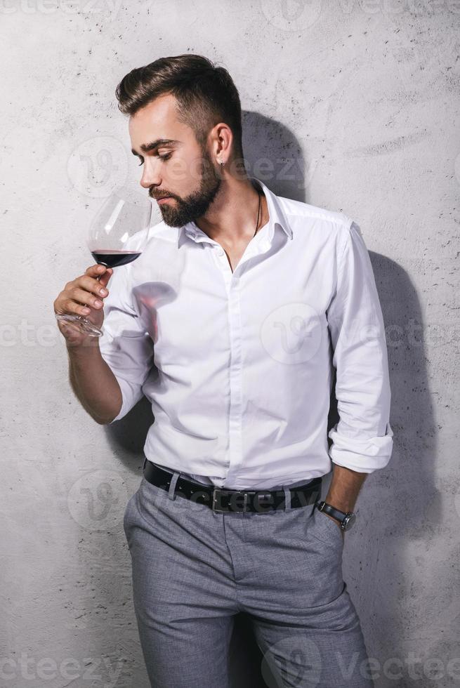 homem barbudo bonito está provando vinho tinto foto