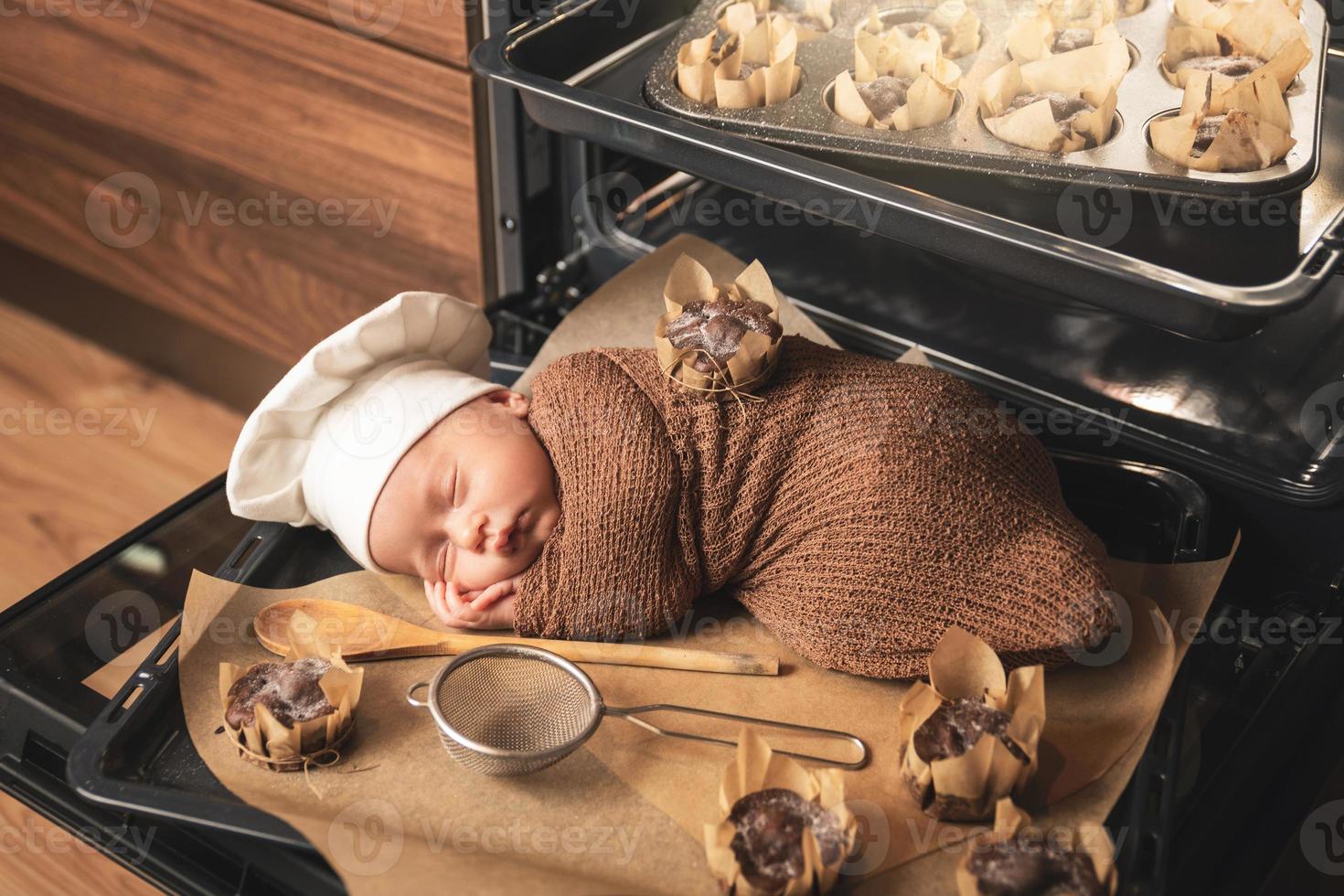 bebê recém-nascido com chapéu de chef está deitado na bandeja do forno com muffins foto