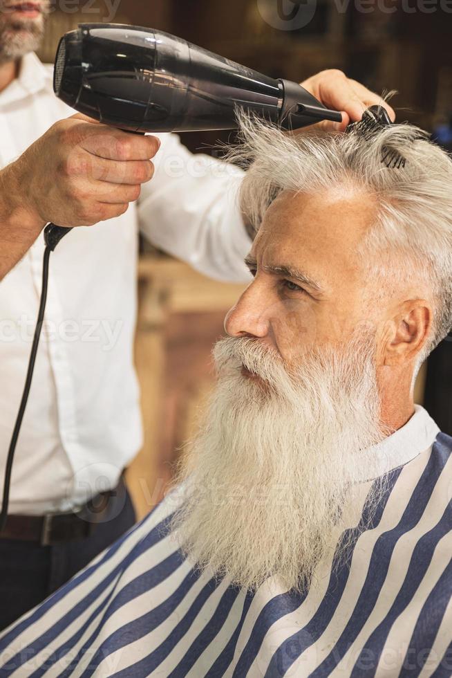 cabeleireiro fazendo corte de cabelo elegante para um velho bonito foto