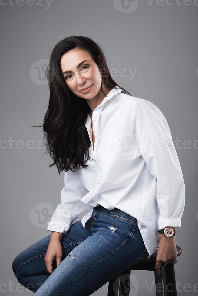 bela modelo de moda de meia idade vestindo jeans e camisa branca em um estúdio de fotografia foto