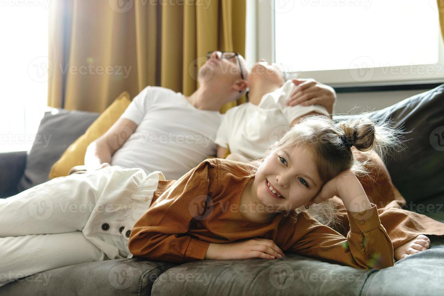 menina feliz assistindo desenhos animados com seus pais cansados foto