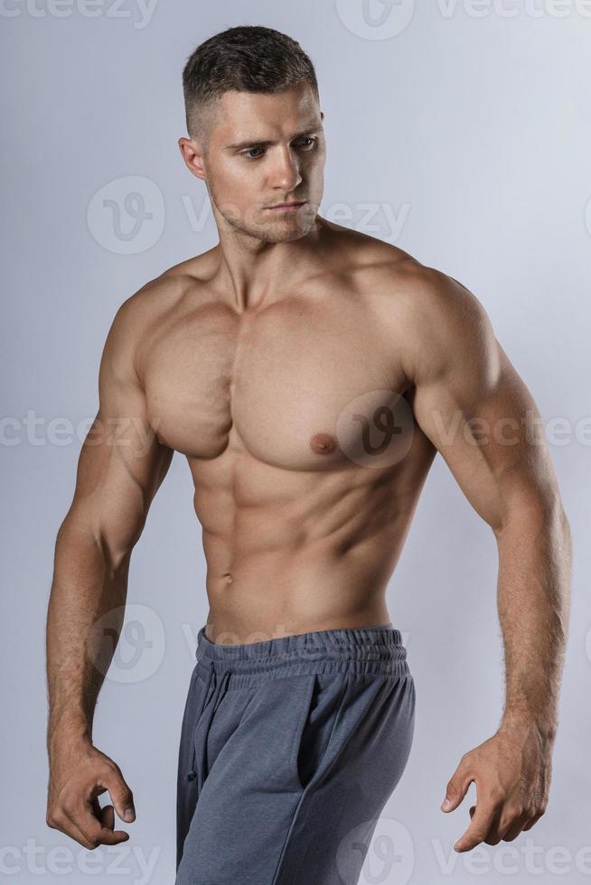fisiculturista mostrando seu corpo musculoso contra um fundo cinza foto