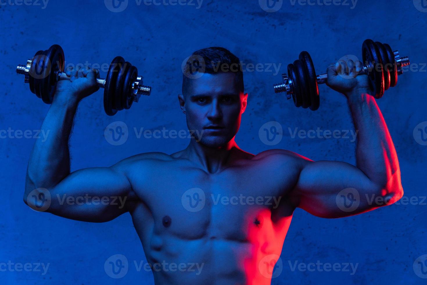 homem musculoso fisiculturista exercitando com halteres em luz neon colorida foto