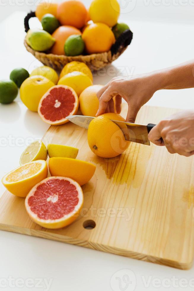 mãos femininas com faca cortando frutas cítricas na tábua para suco fresco caseiro foto