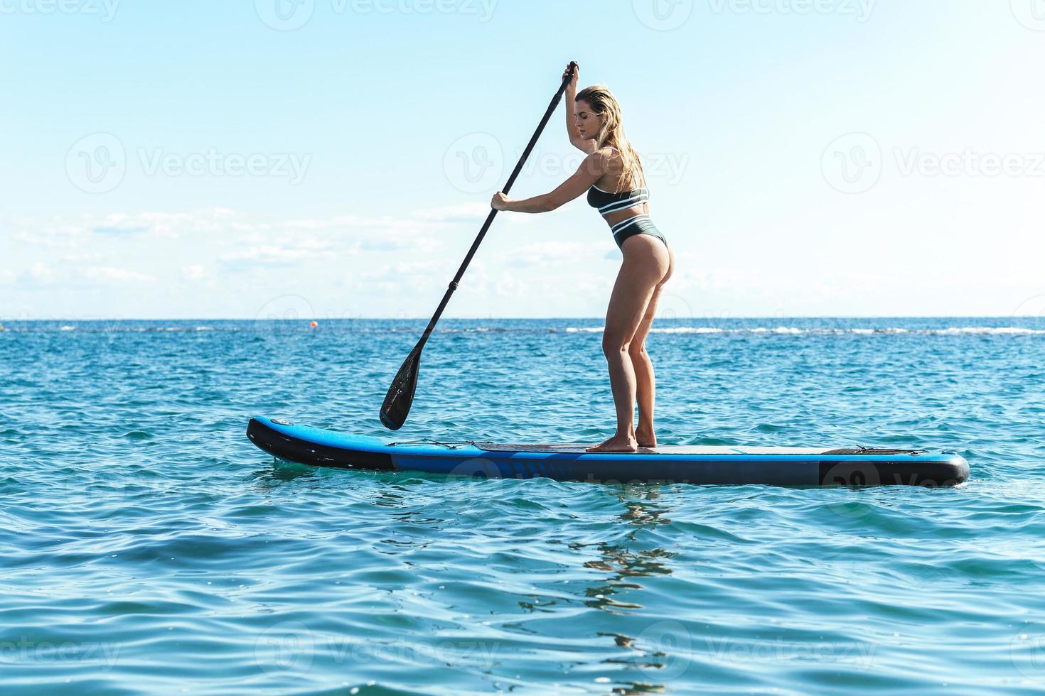 jovem surfista feminina de biquíni andando de stand-up paddle no oceano. foto