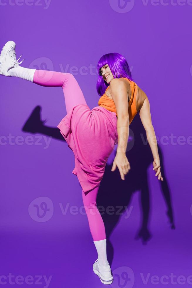 dançarina despreocupada vestindo roupas esportivas coloridas atuando contra fundo roxo foto