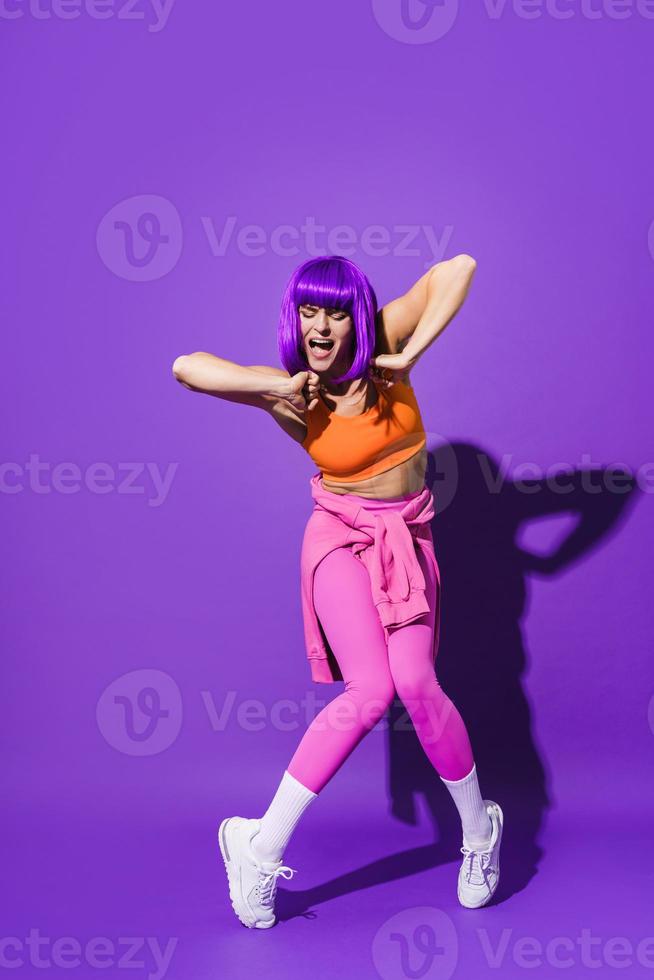 dançarina despreocupada vestindo roupas esportivas coloridas atuando contra fundo roxo foto