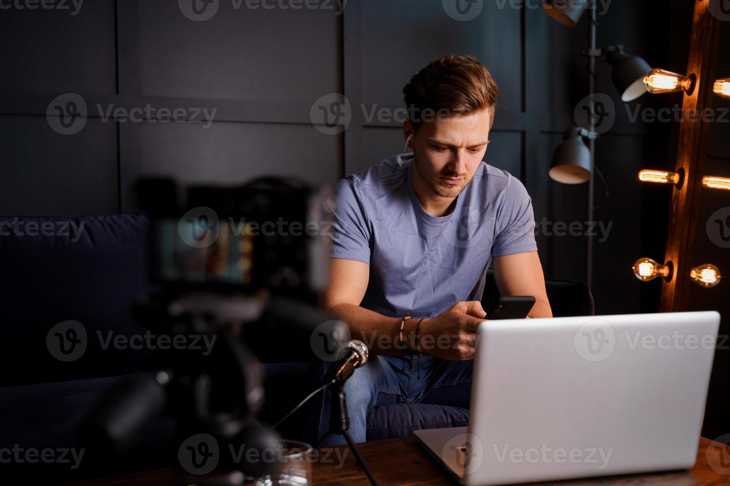 jovem blogueiro está usando seu telefone na frente de um laptop foto