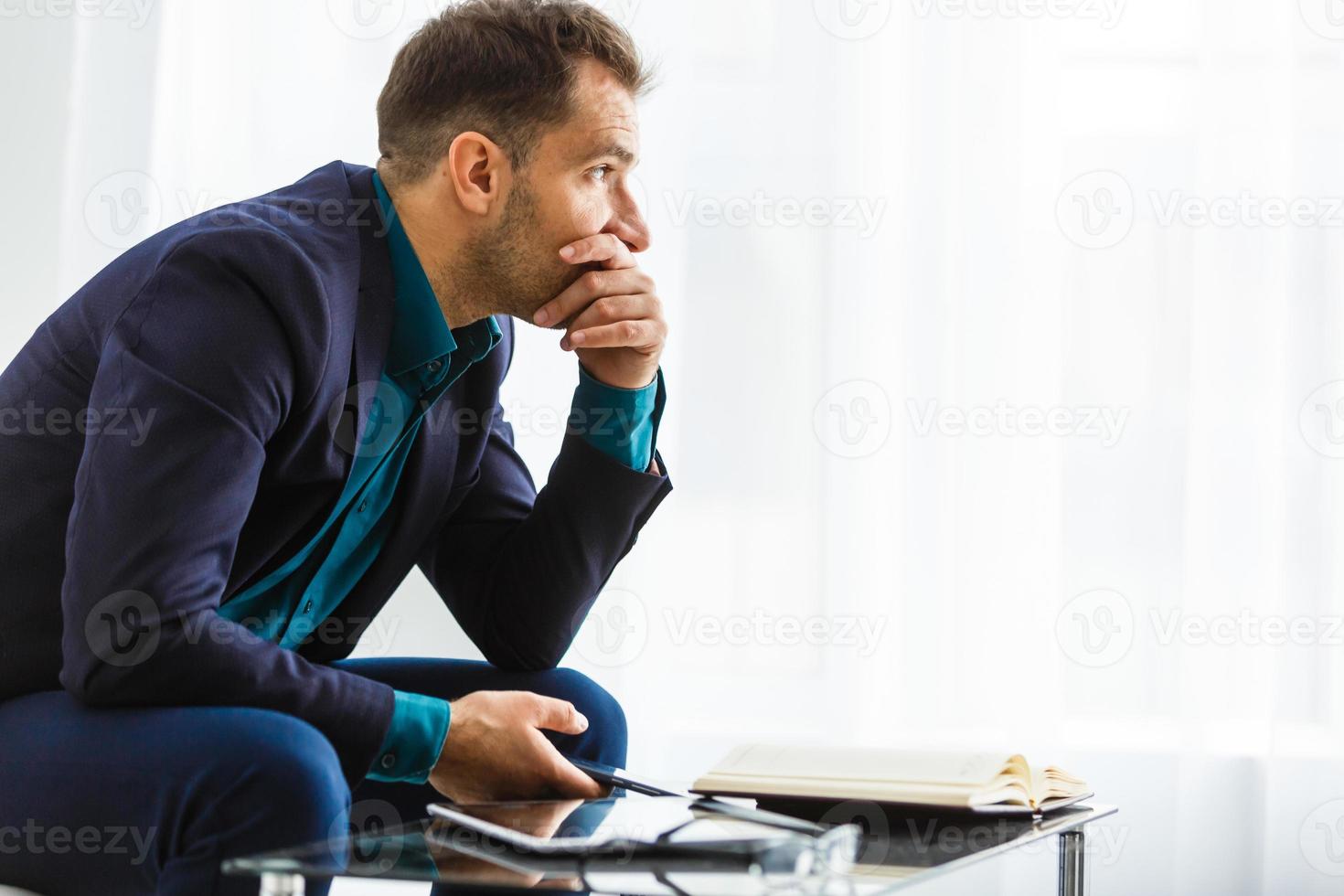 retrato de um jovem empresário bonito sentado em um sofá moderno, segurando um tablet digital e sorrindo amplamente para a câmera foto