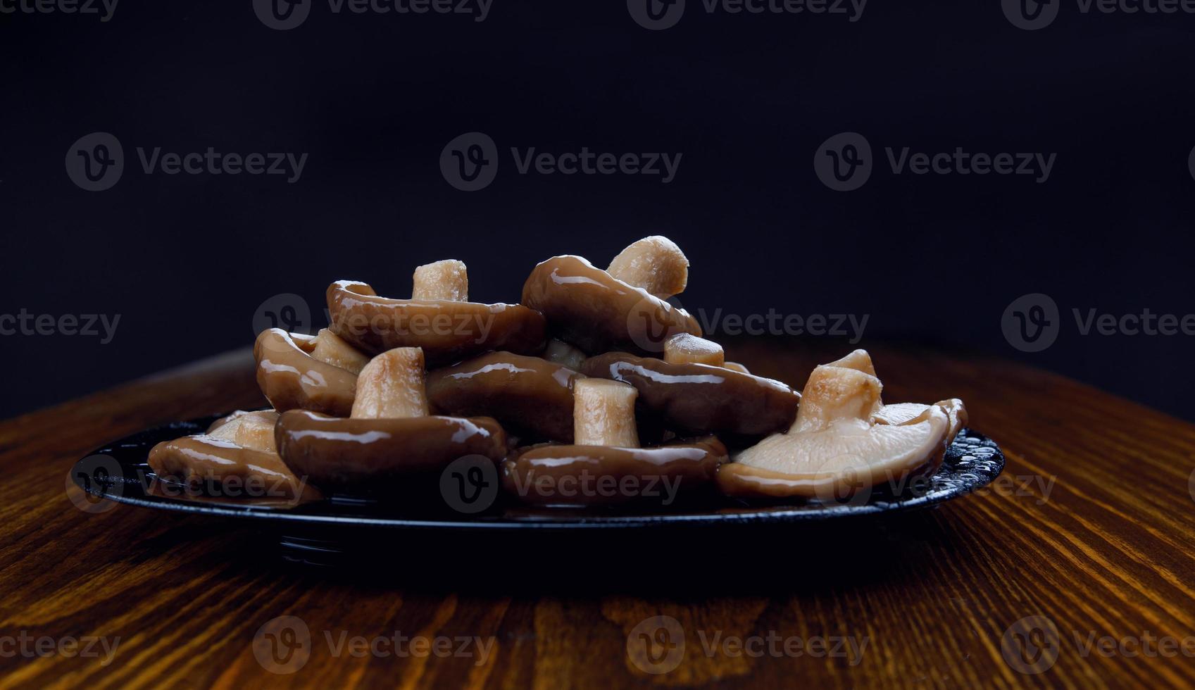 uma pilha de cogumelos em conserva em um prato preto sobre uma mesa de madeira. comida saudável da aldeia. foto