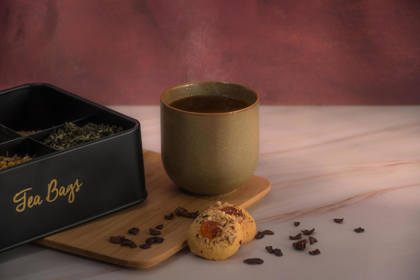 uma xícara de chá e diferentes folhas de chá com biscoitos em uma mesa foto
