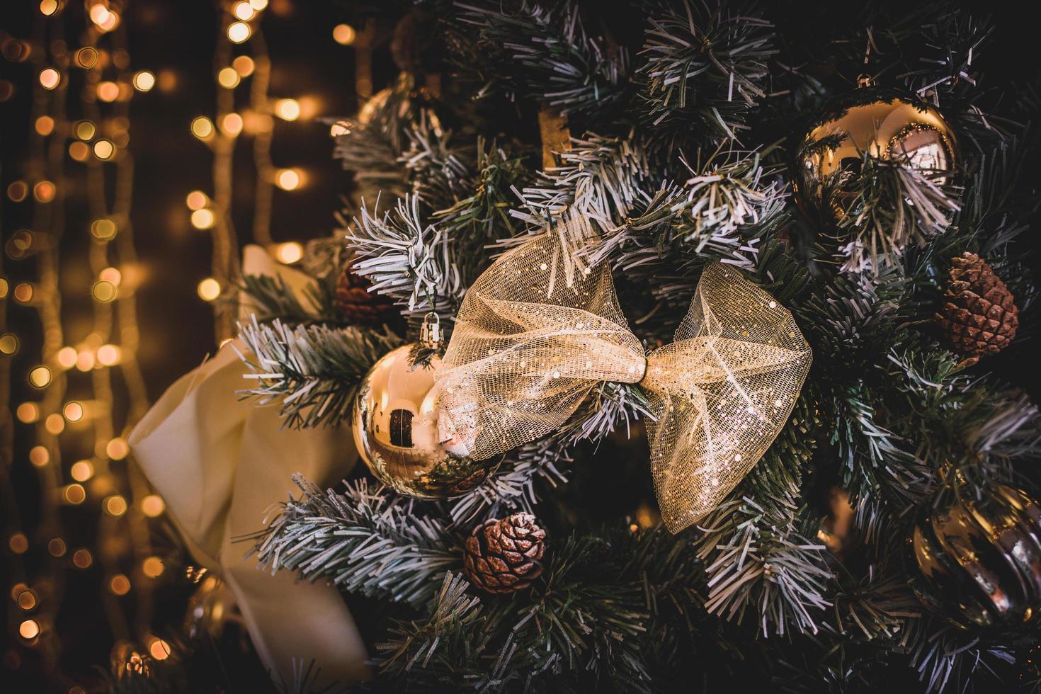 um close-up de enfeites de natal dourados e pinhas pendurados em uma árvore com um bokeh de fundo foto