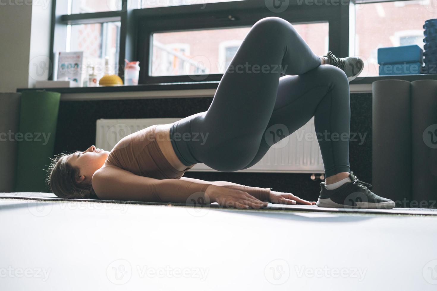 jovem morena fazendo alongamento pilates, praticar ioga na esteira no clube de fitness foto
