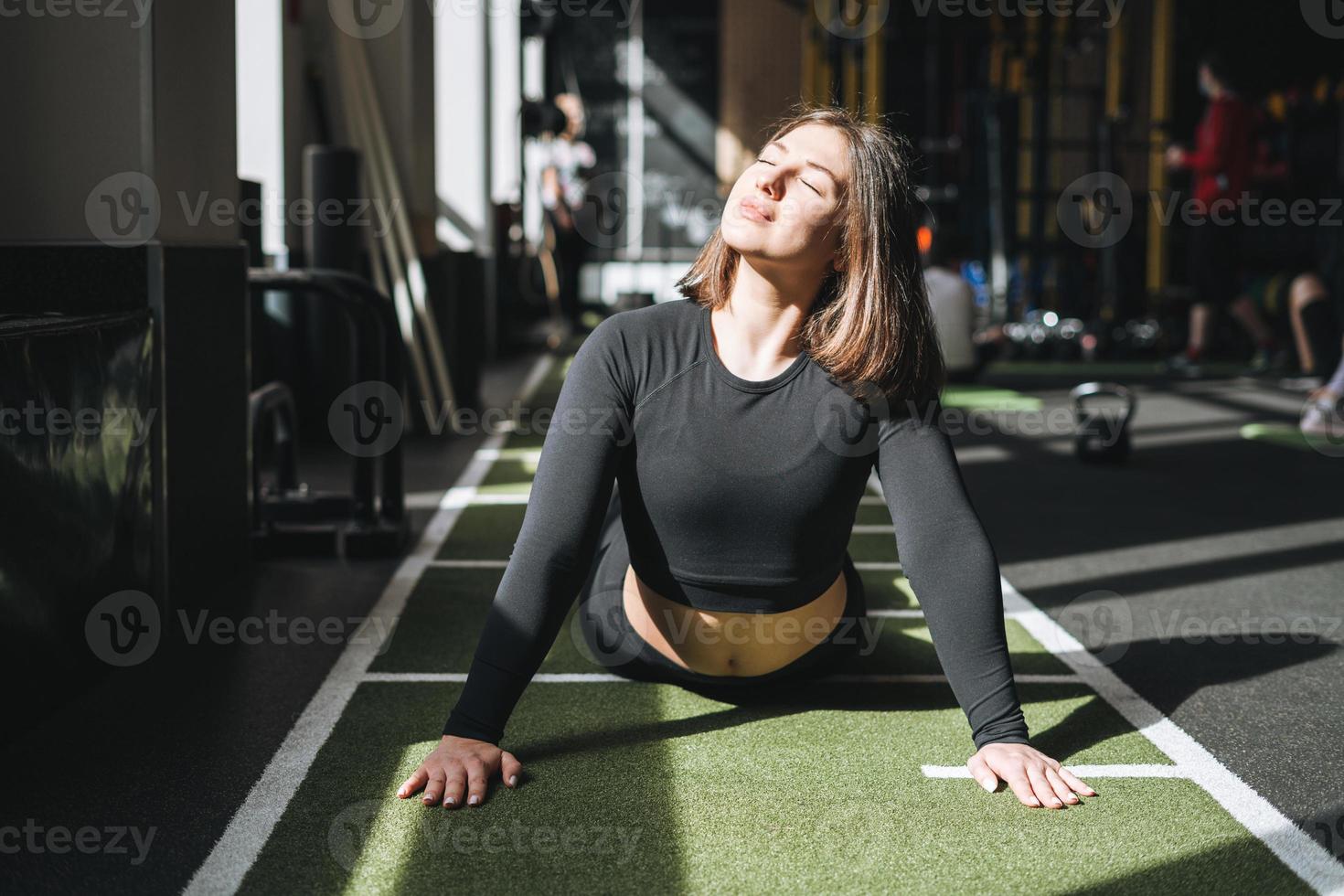 jovem morena fazendo alongamento pilates, pratica ioga na esteira no ginásio do clube de fitness foto