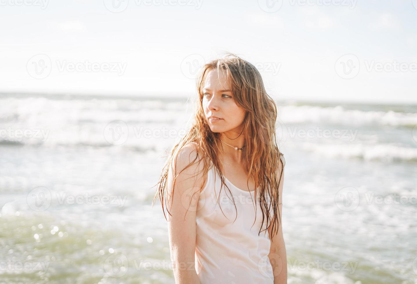 jovem mulher bonita loira com cabelos longos em vestido branco curtindo a vida na praia do mar foto