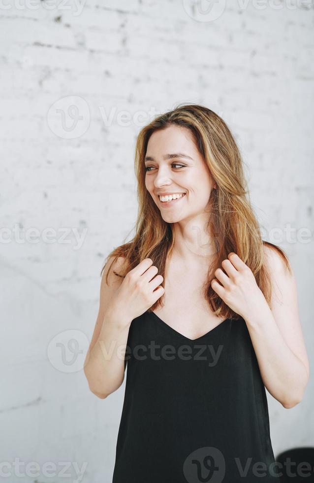 retrato da beleza da moda de uma jovem feliz com cabelos longos na noite elegante vestido preto no interior branco foto