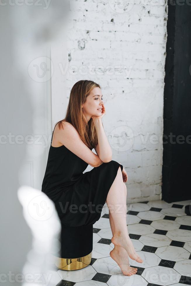 retrato da beleza da moda de uma jovem feliz com cabelos longos na noite elegante vestido preto no interior branco foto