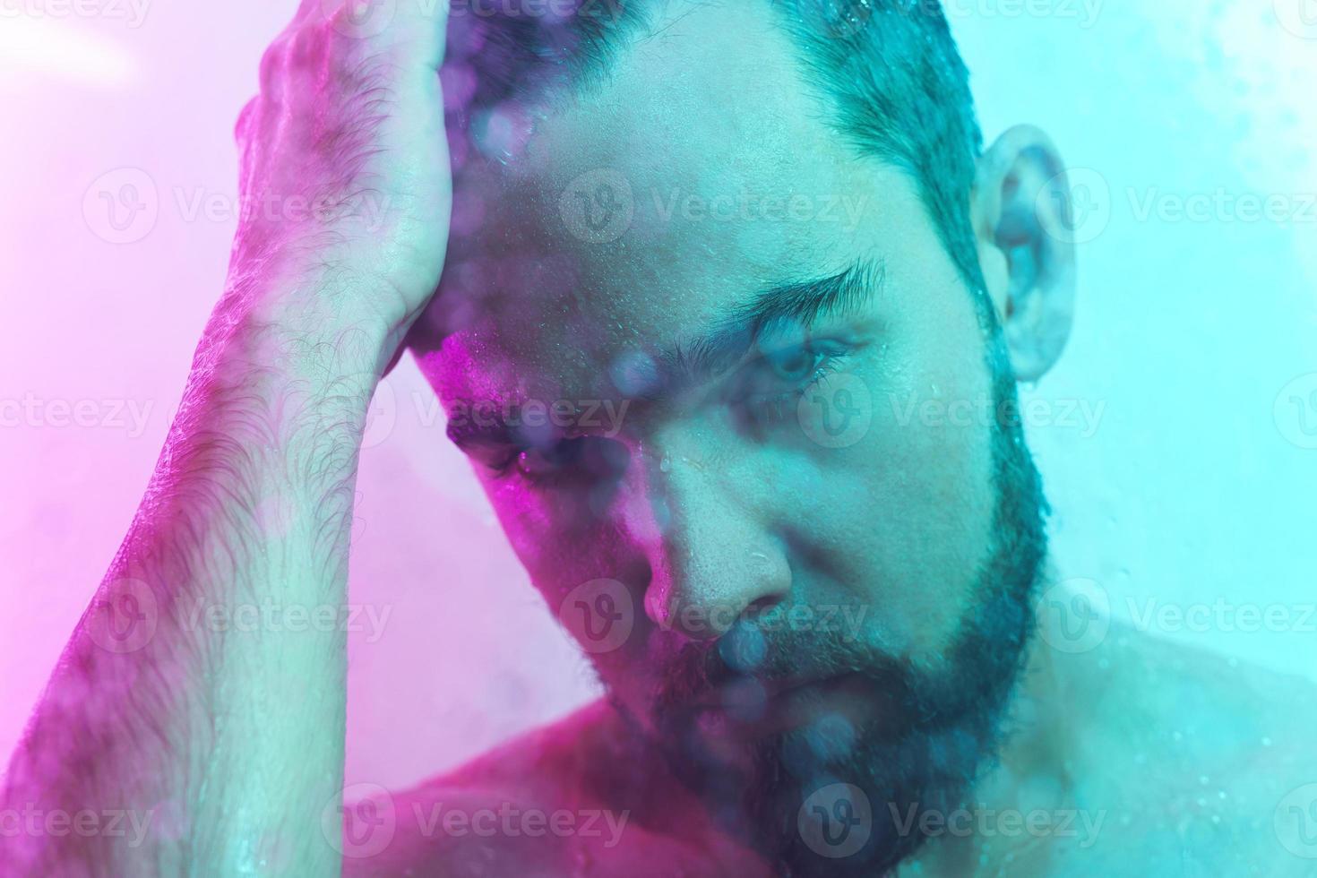 retrato de jovem bonito capturado através de vidro molhado em luz colorida foto