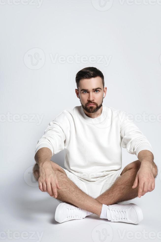 homem bonito vestindo moletom branco e shorts com fones de ouvido sem fio sentado foto