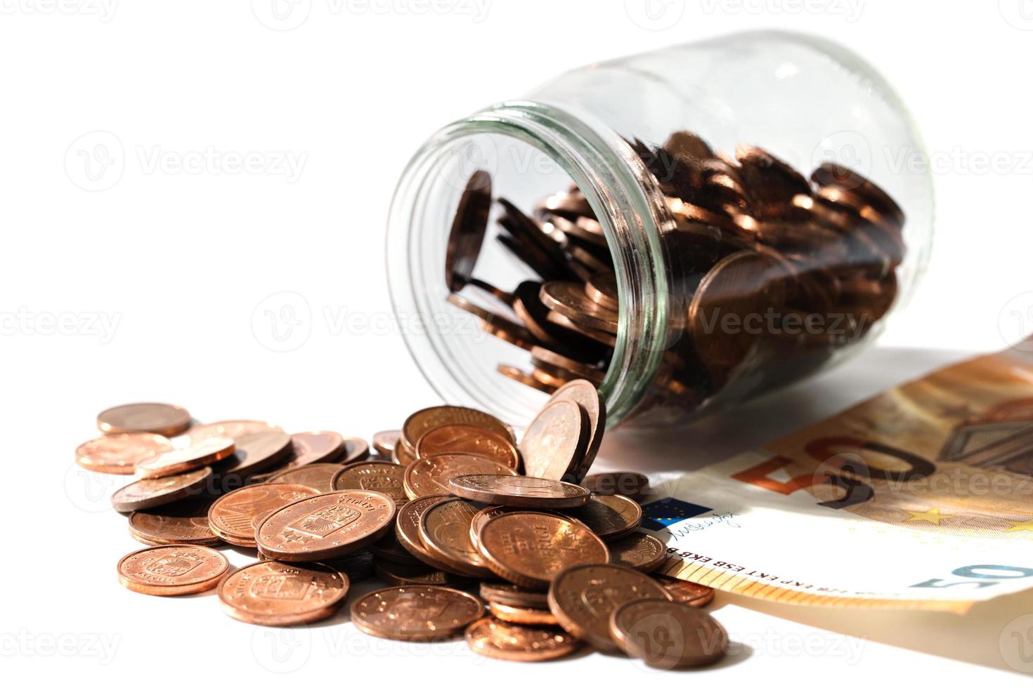 notas de cinquenta euros e moedas de baixo valor de cobre brilhante derramadas de uma jarra de vidro. foto