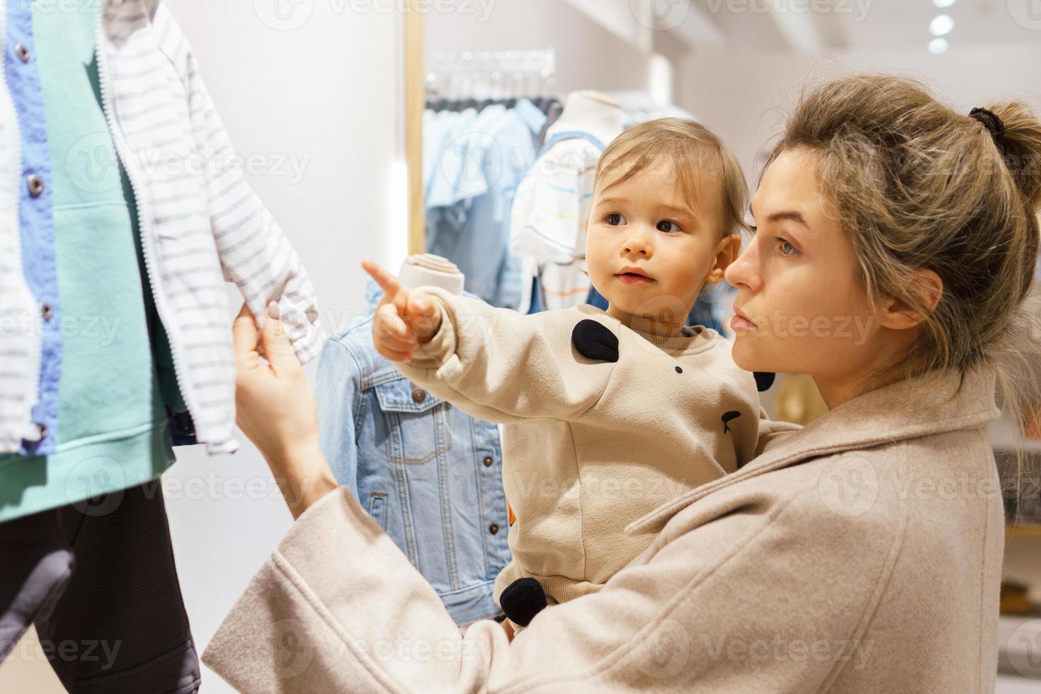 mulher com seu filho bebê escolhendo roupas em loja de roupas foto